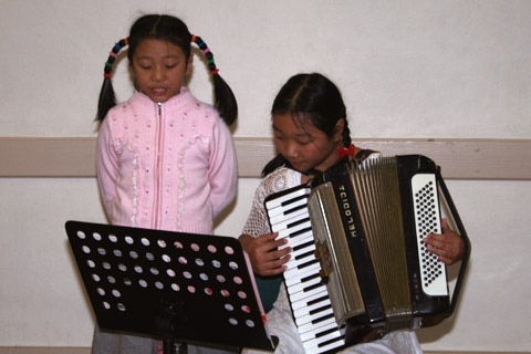 Marina Jin singing and Jessica Jin playing the accordion.